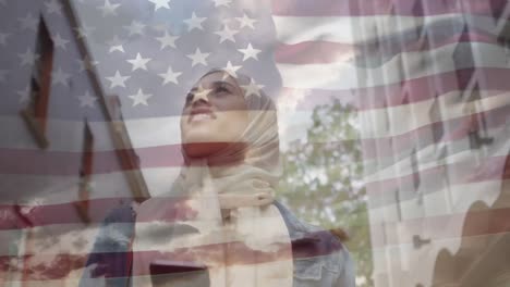 Animation-of-American-flag-waving-over-woman-in-hijab-walking-holding-smartphone