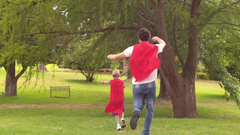 Wow-text-on-speech-bubble-against-dad-and-son-in-superhero-costume-running-in-a-garden