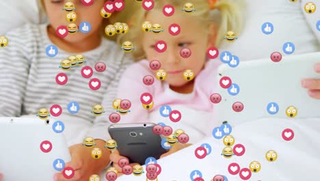 Multiple-face-emojis-floating-against-kids-using-electronic-devices-in-bed