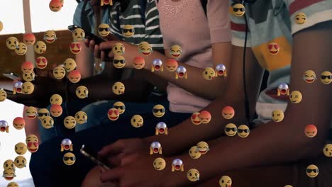 Emojis-De-Múltiples-Caras-Flotando-Contra-Un-Grupo-De-Estudiantes-Que-Usan-Teléfonos-Inteligentes