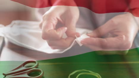 Die-Ungarische-Flagge-Weht-Gegen-Den-Mittelteil-Einer-Frau,-Die-Eine-Gesichtsmaske-Näht