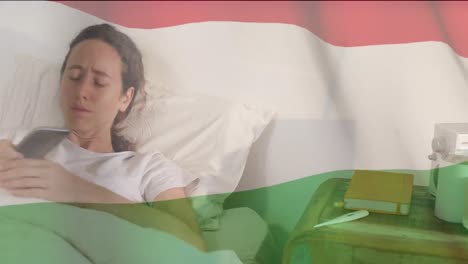 Ungarische-Flagge-Weht-Gegen-Frau,-Die-Hustet,-Während-Sie-Im-Bett-Ihr-Smartphone-Benutzt