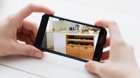 Person-holding-smartphone-with-modern-kitchen-interiors-displayed-on-screen