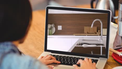 Woman-using-laptop-with-modern-kitchen-interiors-displayed-on-screen