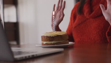 Frau-Bläst-Kerze-Auf-Den-Kuchen,-Während-Sie-Zu-Hause-Einen-Videochat-Auf-Ihrem-Laptop-Führt