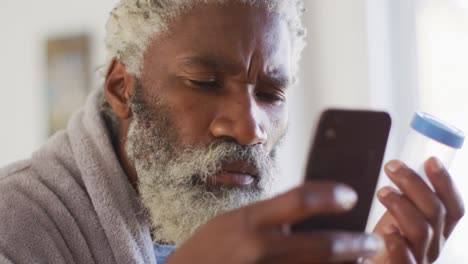 Älterer-Mann-Benutzt-Smartphone,-Während-Er-Leeren-Medikamentenbehälter-In-Der-Hand-Hält