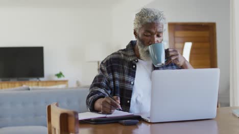 Senior-man-drinking-coffee-while-taking-notes