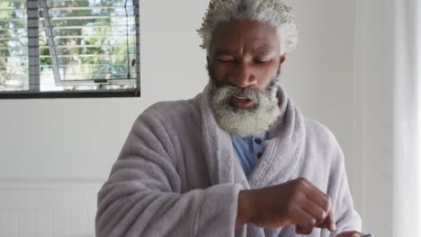 Senior-man-sneezing-while-using-smartphone-at-home