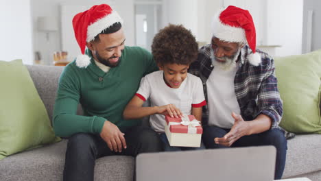 Vater,-Sohn-Und-Großvater-öffnen-Die-Geschenkbox,-Während-Sie-Einen-Videochat-Auf-Dem-Laptop-Führen