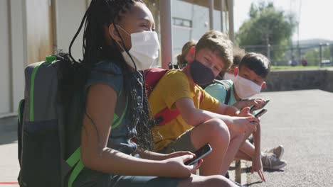 Gruppe-Von-Kindern,-Die-Gesichtsmasken-Tragen-Und-Smartphones-Benutzen,-Während-Sie-Zusammensitzen