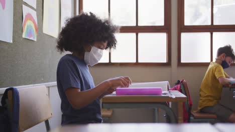 Boy-wearing-face-mask-sneezing-while-sitting-on-his-desk-at-school-