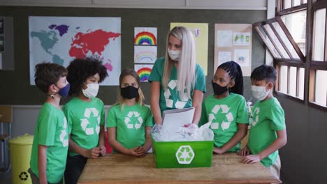 Lehrerin-Und-Gruppe-Von-Kindern-Mit-Gesichtsmasken-Und-Recyclingbehälter-In-Der-Schule