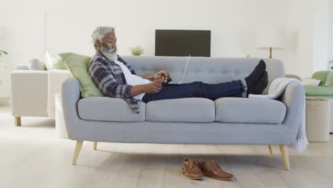 Senior-man-talking-on-smartphone-while-using-laptop-at-home