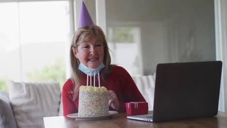 Ältere-Frau-Bläst-Kuchen,-Während-Sie-Zu-Hause-Einen-Video-Chat-Auf-Dem-Laptop-Führt