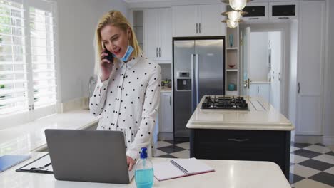 Frau-Spricht-Auf-Dem-Smartphone,-Während-Sie-In-Der-Küche-Einen-Laptop-Benutzt