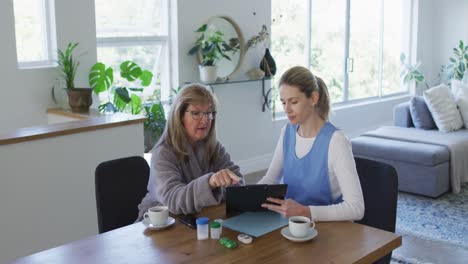 Female-health-worker-and-senior-woman-discussing-over-clipboard-at-home
