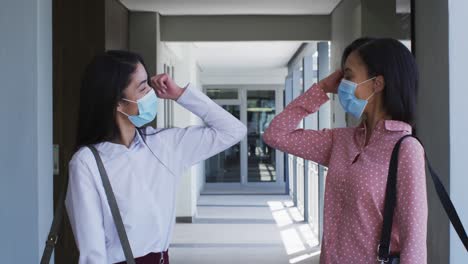 Zwei-Frauen-Mit-Gesichtsmasken-Begrüßen-Sich-Im-Büro,-Indem-Sie-Ihre-Ellbogen-Berühren