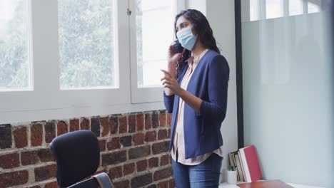 Woman-wearing-face-mask-talking-on-smartphone-at-office