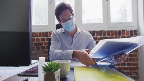 Man-wearing-face-mask-looking-at-documents-at-office