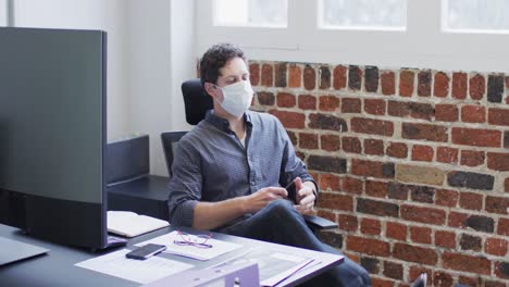 Man-wearing-face-mask-sitting-on-his-desk-at-office