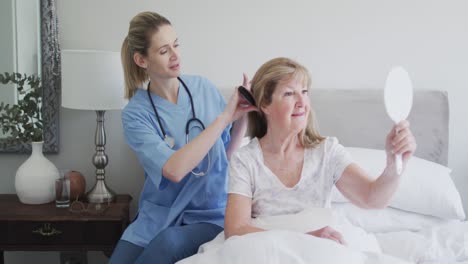 Female-health-worker-brushing-hair-of-senior-woman-at-home
