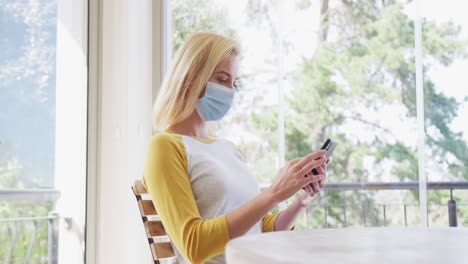 Woman-wearing-face-mask-using-smartphone-at-home