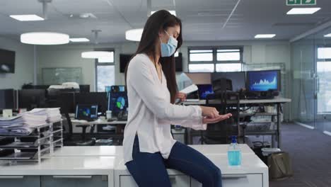 Woman-wearing-face-mask-sanitizing-her-hands-at-office