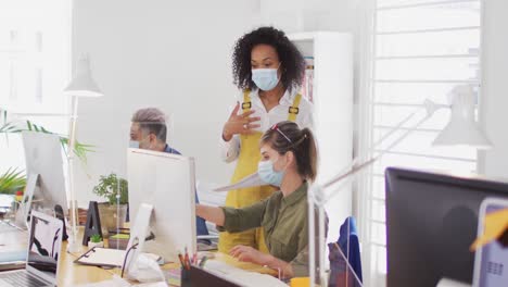 Office-colleagues-wearing-face-masks-discussing-over-computer-at-office