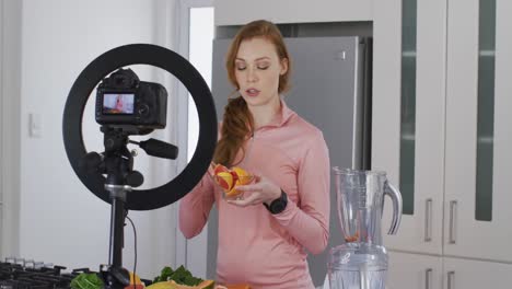 Woman-holding-a-bowl-of-chopped-fruit-and-recording-it-with-digital-camera-in-the-kitchen