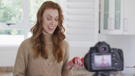 Woman-talking-while-holding-tomatoes-and-recording-it-with-digital-camera-in-the-kitchen