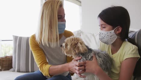Mother-and-daughter-wearing-face-masks-playing-with-their-pet-dog-at-home