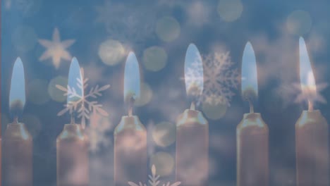 Snowflakes-moving-against-burning-candles-on-blue-background
