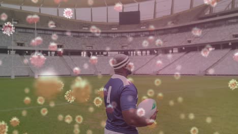 Covid-19-cells-against-male-rugby-player-holding-rugby-ball-on-sports-field
