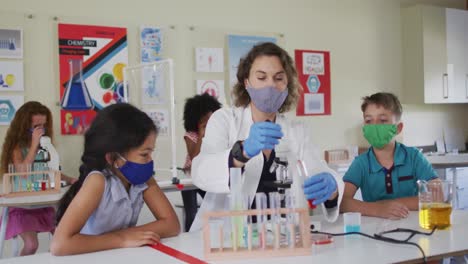 Female-teacher-wearing-face-mask-and-protective-glasses-teaching-students-in-laboratory