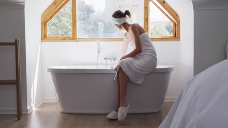 Caucasian-woman-spending-time-at-home,-sitting-on-edge-of-bathtub-running-a-bath,-slow-motion.-Socia