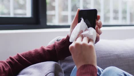 Mid-section-of-woman-wiping-her-smartphone-with-a-tissue