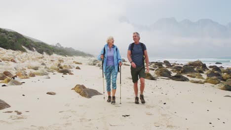 Senior-hiker-couple-with-backpack-and-hiking-poles-talking-to-each-other-and-walking-while-hiking