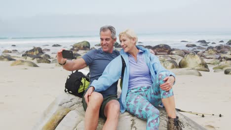 Senior-hiker-couple-with-backpack-and-hiking-poles-taking-a-selfie-from-smartphone