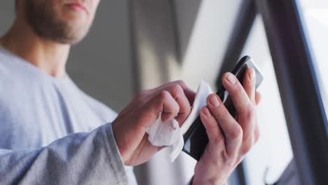 Mid-section-of-caucasian-man-cleaning-smartphone-with-tissue-in-slow-motion