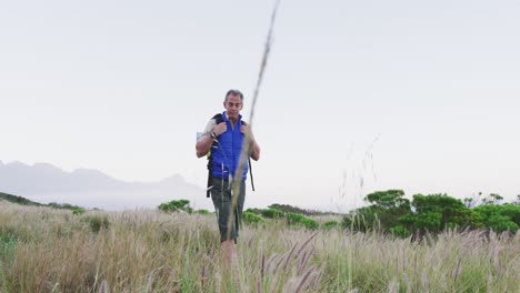 Senior-hiker-man-with-backpack-walking-and-touching-wild-grass-on-the-grass-field-in-the-mountains.-