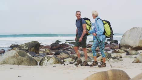 Senior-hiker-couple-with-backpack-and-hiking-poles-talking-to-each-other-and-walking-while-hiking