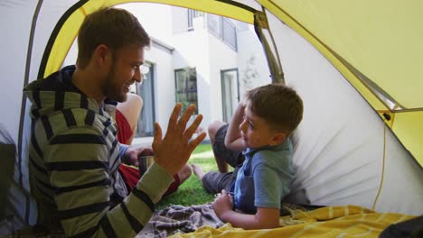 Caucasian-man-lying-in-a-tent-with-his-son-in-the-garden-talking-and-high-fiving