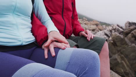 Mid-section-of-senior-hiker-couple-with-backpacks-sitting-on-the-rocks