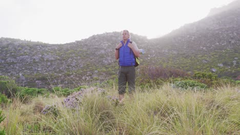 Senior-hiker-man-with-backpack-standing-on-the-grass-field-in-the-mountains.-trekking