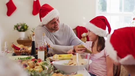 Caucasian-senior-man-in-santa-hat-wiping-his-daughter-face-with-tissue-sitting-on-dining-table-and-e