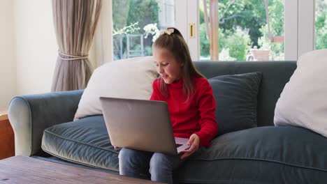 Kaukasisches-Mädchen-Benutzt-Laptop,-Während-Es-Zu-Hause-Auf-Der-Couch-Im-Wohnzimmer-Sitzt