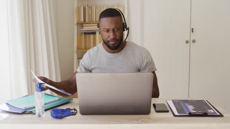 African-american-man-in-home-wearing-phone-headset-using-laptop