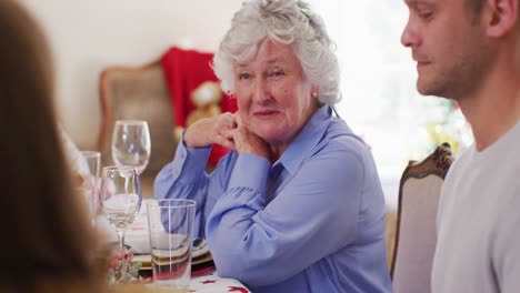 Caucasian-senior-woman-talking-while-sitting-on-dining-table