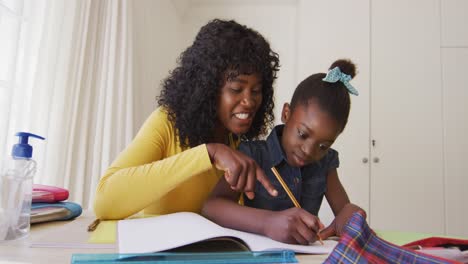 Afroamerikanische-Mutter-Hilft-Ihrer-Tochter-Bei-Den-Hausaufgaben,-Während-Sie-Zu-Hause-Sitzt