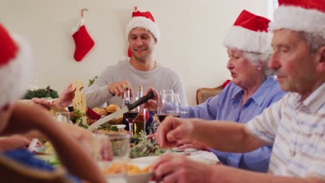 Caucasian-family-in-santa-hats-sitting-on-dining-table